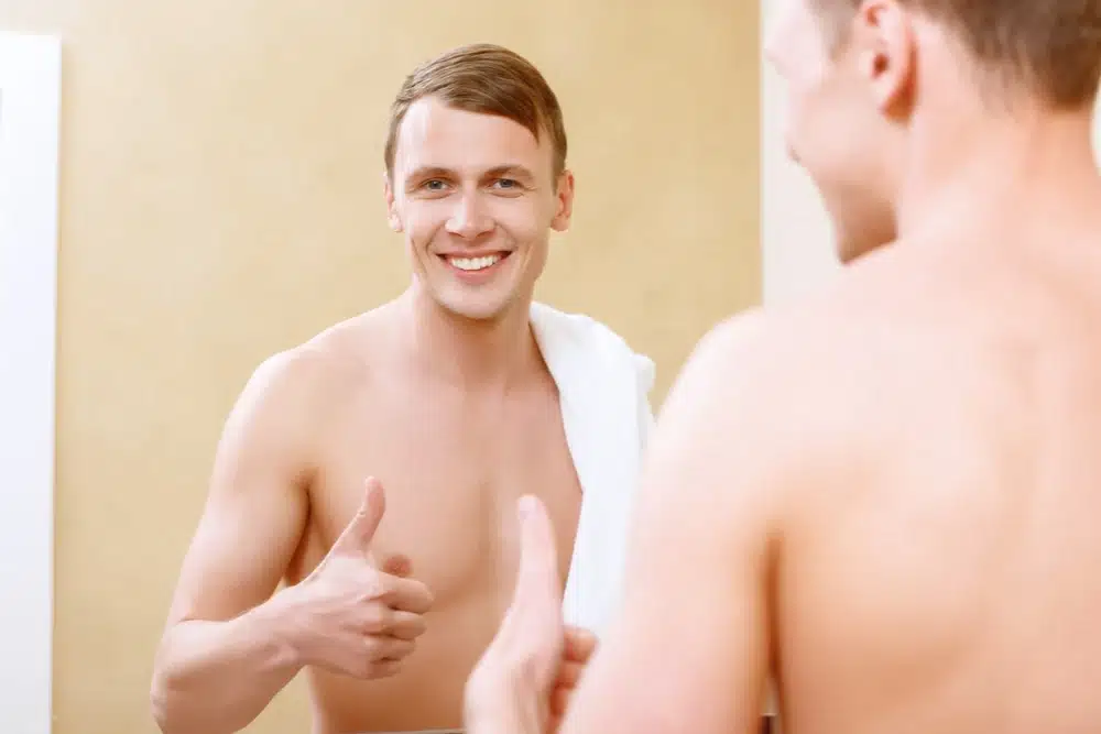 Elégedett szőrtelen mellkasú férfi a tükörbe néz